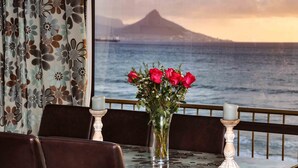A dining table with a vase of red roses, two candles, and a view of the ocean and a mountain. - Witsand 401 by CTHA (Cape Town)