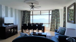 A living room with a TV, a ceiling fan, a dining area with chairs, and a sofa. - Witsand 401 by CTHA (Cape Town)