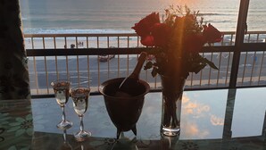 A table with a vase of roses, a champagne bottle, and two glasses, overlooking a beach with a sunset and ships in the distance. - Witsand 401 by CTHA (Cape Town)