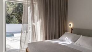 A bedroom with a bed, a bedside table with a lamp, and a view of the outdoors.