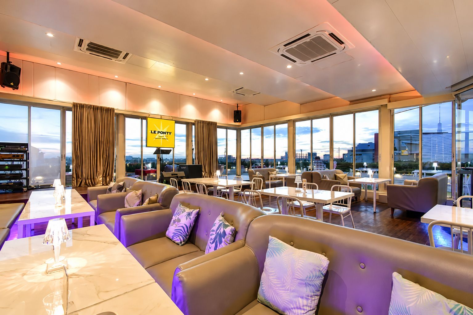 A modern hotel lobby with leather seating, a bar area, and large windows offering city views.