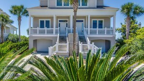 Une maison à deux étages située en bord de mer, dotée d’un balcon, d’un escalier et d’un palmier au premier plan.