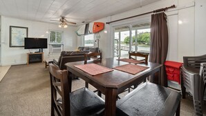 Ein Essbereich mit Holztisch und Stühlen, einem Deckenventilator und einem Fernseher im Hintergrund.