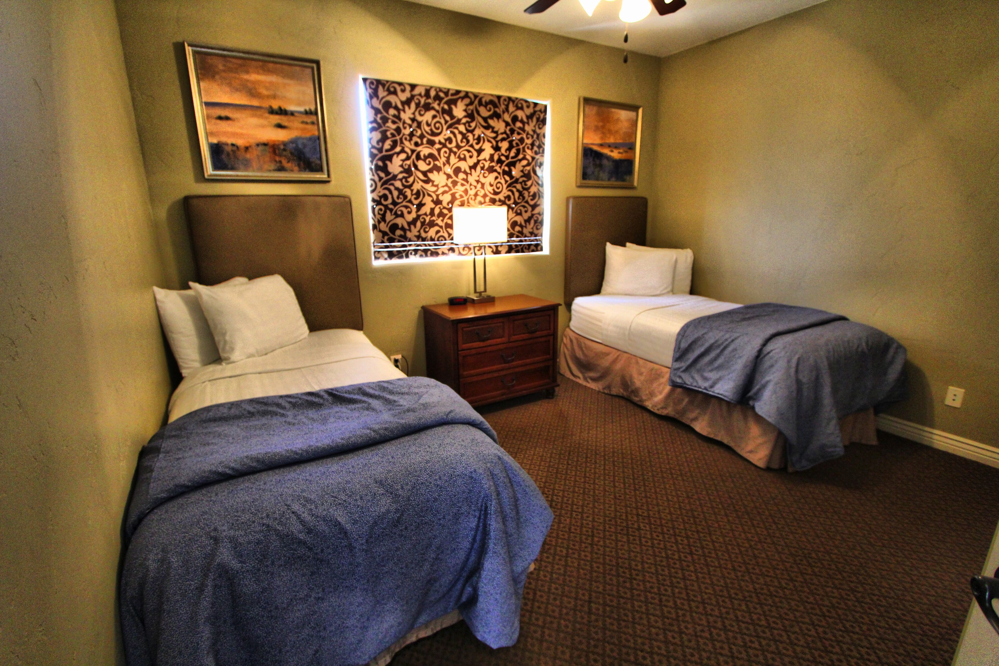 A hotel room with two beds, a nightstand, a lamp, and a patterned wall.