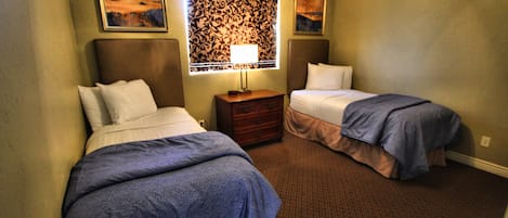 A hotel room with two beds, a nightstand, a lamp, and a patterned wall.