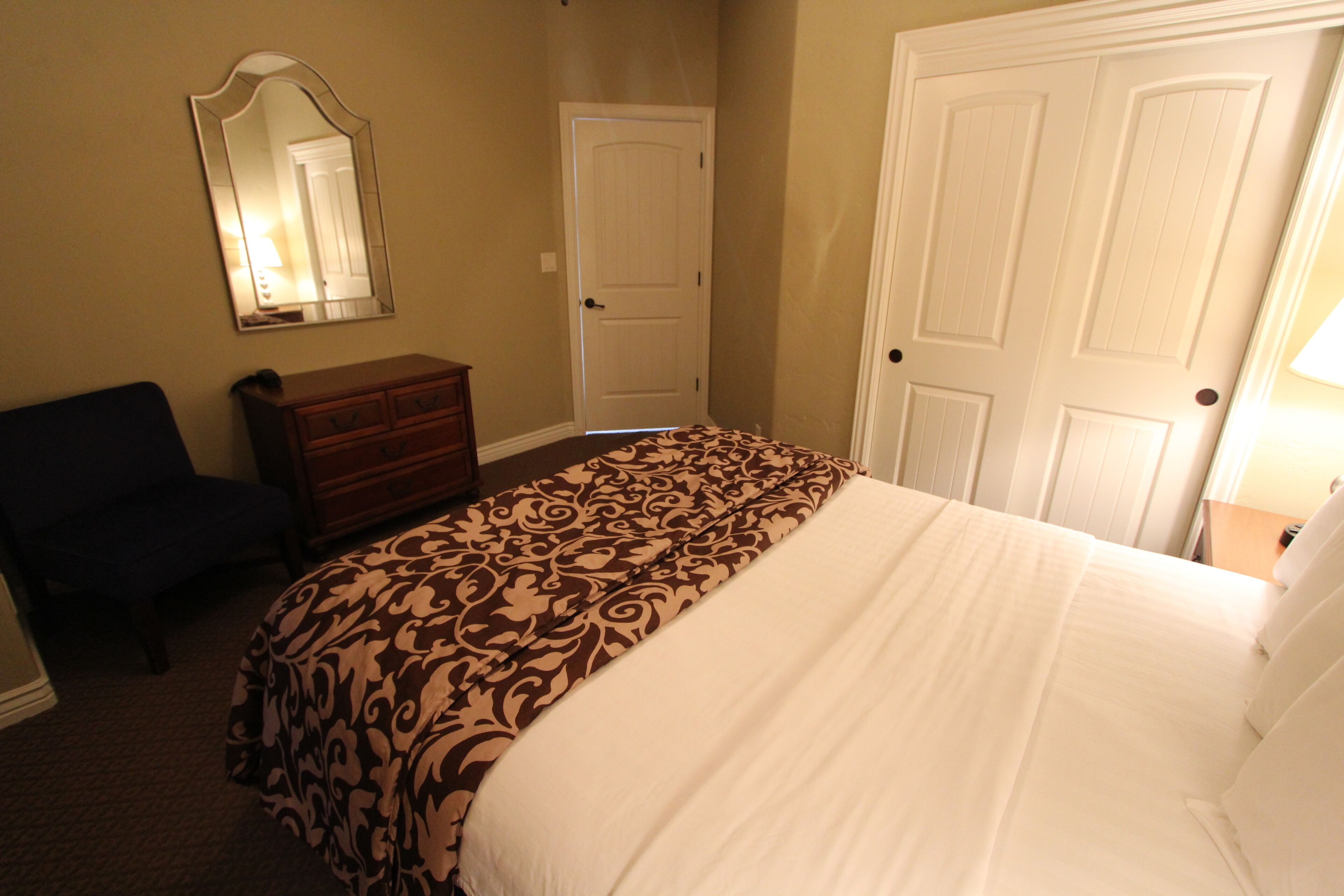 A bedroom with a bed, a dresser, a chair, and two doors.