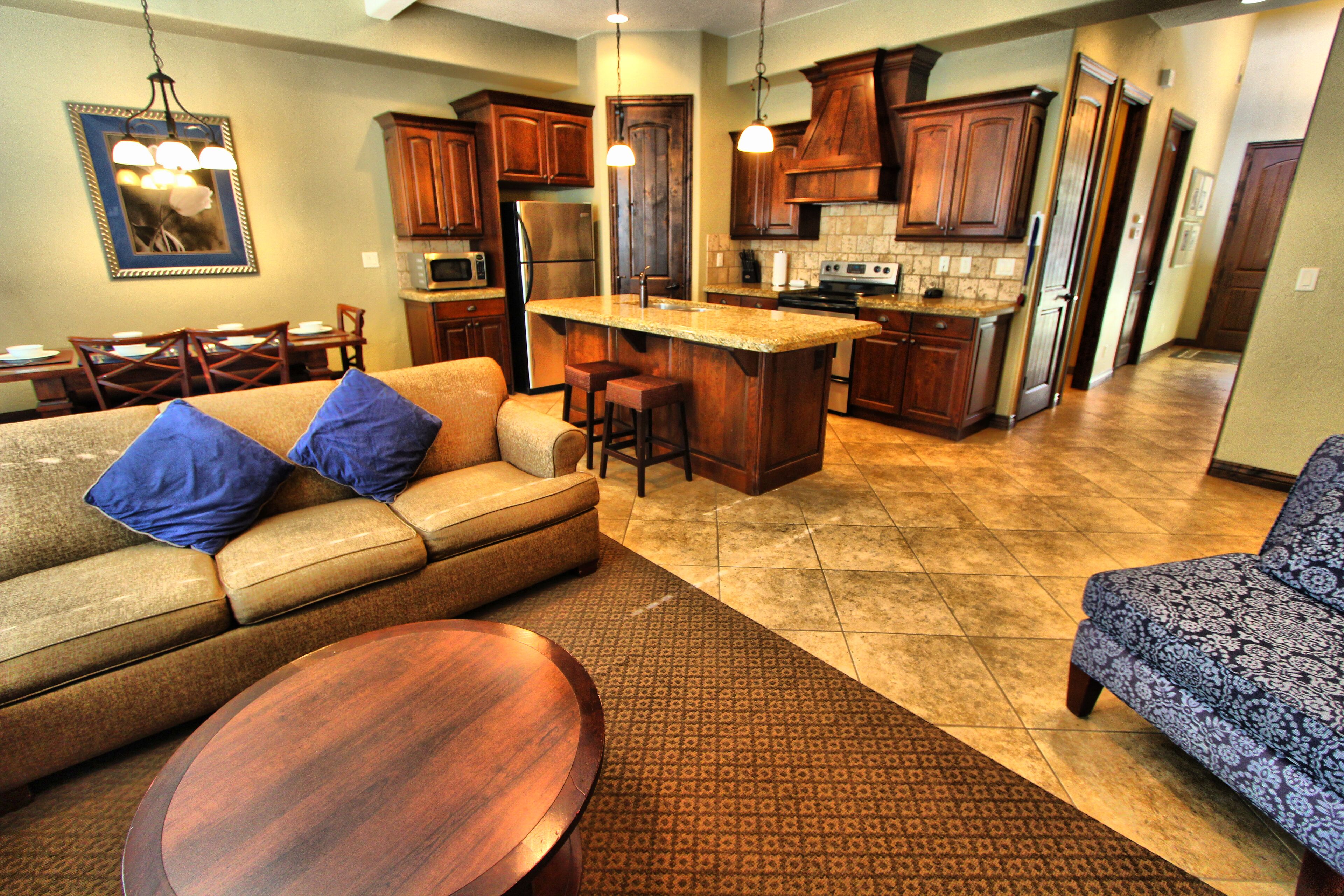 A modern kitchen with wooden cabinets, a central island, and a dining area with a sofa and chairs.