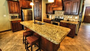A kitchen with granite countertops, stainless steel appliances, wooden cabinets, and a bar stool. - Canyon Villas at Coral Ridge (Washington)