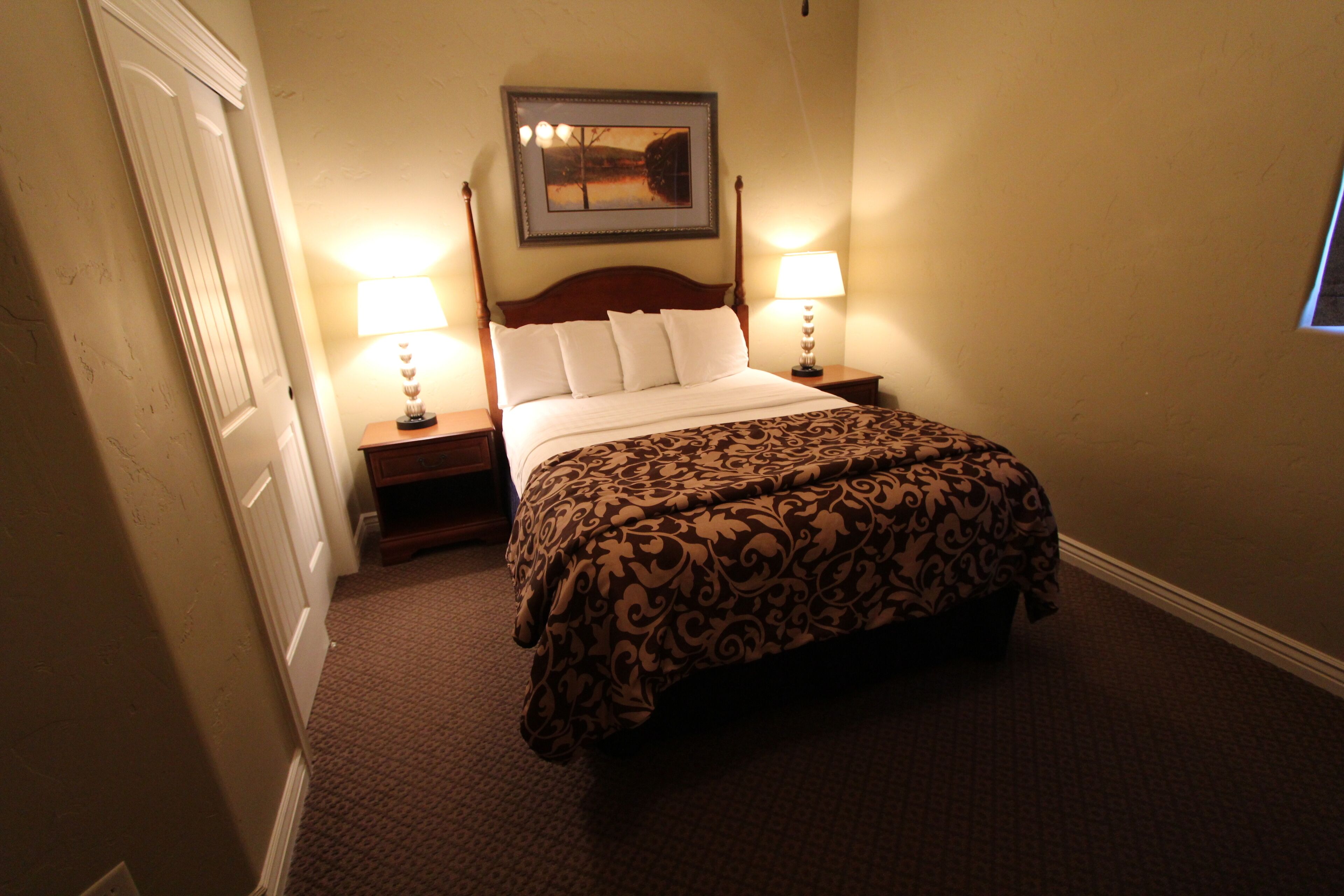 A hotel room with a bed, two bedside lamps, a framed picture on the wall, and a door.