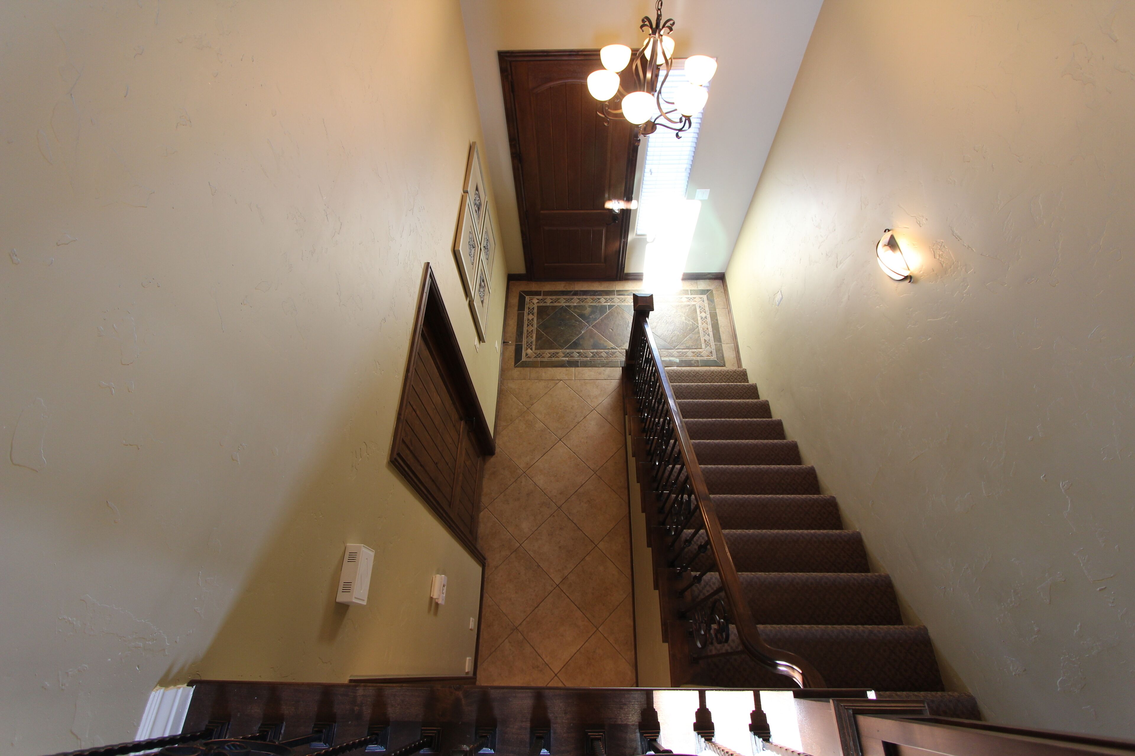 A staircase with a wooden handrail, a wall-mounted light fixture, and a decorative tile pattern at the base.