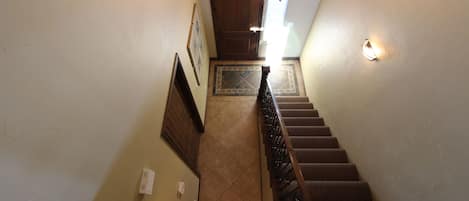 A staircase with a wooden handrail, a wall-mounted light fixture, and a decorative tile pattern at the base.