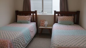 Une chambre avec deux lits simples, chacun agrémenté de draps et d’oreillers à motifs, une petite table de chevet avec une lampe et une fenêtre avec des stores.
