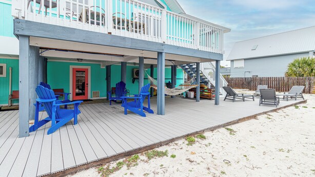 Ein zweistöckiges Haus mit überdachter Veranda, blauen Adirondack-Stühlen, einer Hängematte und einer Treppe, die zum oberen Stockwerk führt.