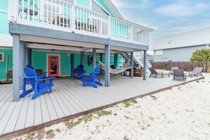 Una casa de dos pisos con un porche cubierto, sillas Adirondack azules, una hamaca y una escalera que conduce al nivel superior.