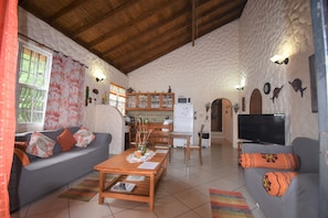 A cozy living room with a sofa, a coffee table, and a TV. There's a kitchen area with cabinets and a refrigerator.