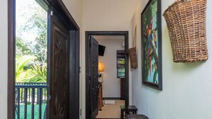 Un pasillo con alfombra de diseño verde y blanco, una cesta de mimbre en la pared y una puerta que da a un espacio exterior con una silla.
