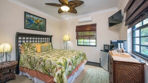Un dormitorio con cama, ventilador de techo, un cuadro, aire acondicionado, televisor, ventana y kitchenette.