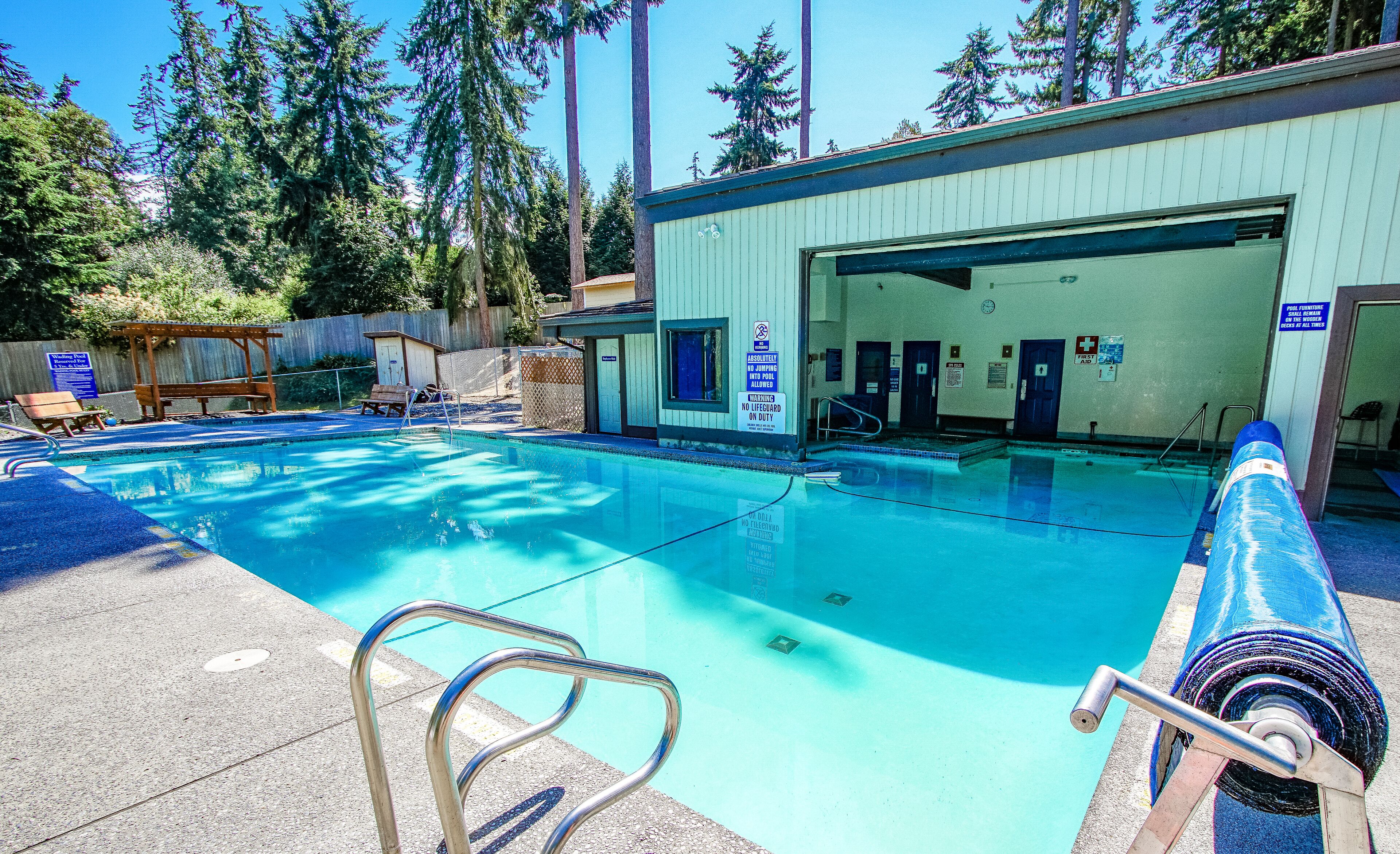 A swimming pool with a lifeguard chair, a pool ladder, and a covered area.