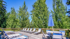 Une terrasse en bois, avec des chaises longues et une table, entourée de grands arbres.
