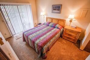 Un dormitorio con una cama grande, dos mesitas de noche con lámparas, un cabecero de madera y vistas al exterior a través de un ventanal corredero.