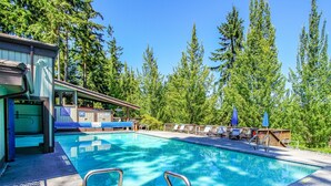 Une piscine avec des marches permettant d’y accéder, entourée de chaises longues et de parasols, avec des arbres en arrière-plan.