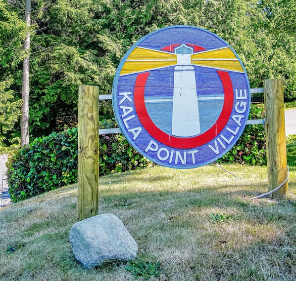 Un letrero circular con el texto 'KALA POINT VILLAGE' y un grabado de un faro.