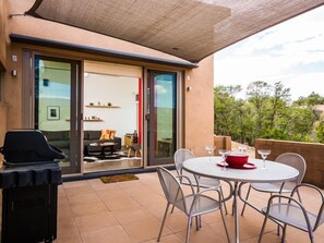 Eine Terrassenfläche mit rundem Tisch und Stühlen, einem Grill und einer Glastür zum Innenbereich.