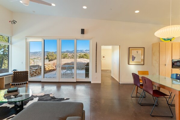 A modern interior with a glass dining table, leather sofa, and a view of mountains through large sliding doors.