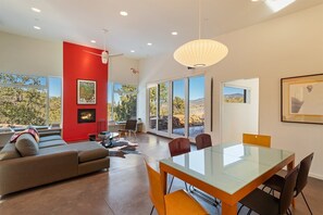 A modern living room with a red accent wall, a fireplace, and large windows offering a view of the outdoors.