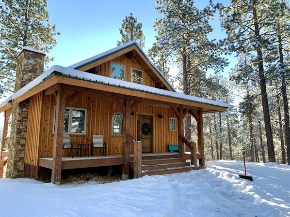 Set amidst a snowy forest, this lodge offers a cozy porch with seating and a welcoming entrance.