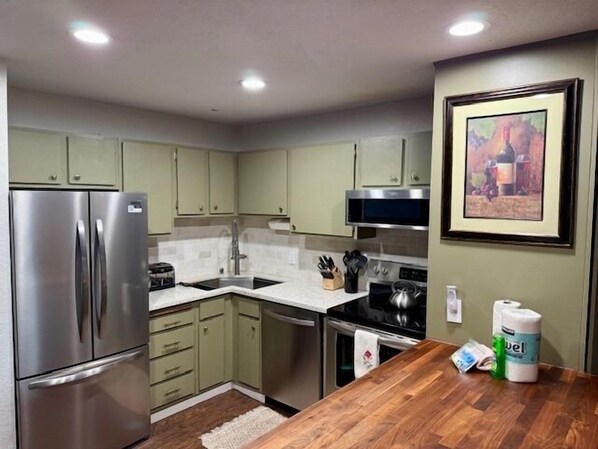 A modern kitchen with green cabinets, stainless steel appliances, a microwave, and a wooden countertop. - Mammoth Ski & Racquet Club #33, 2 Bdrm/2 Baths (Mammoth Lakes)