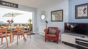 A modern living room with a dining area, a red leather chair, a television, and a view of the sea.