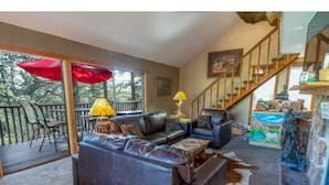 A spacious living room with a leather sofa, a coffee table, and a red umbrella. There is a staircase leading to an upper level, and a painting on the wall. - Rejuvenation Mountian, Estes Park CO (Estes Park)