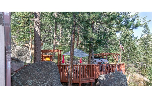 A wooden deck with a metal roof, surrounded by large rocks and trees. - Rejuvenation Mountian, Estes Park CO (Estes Park)