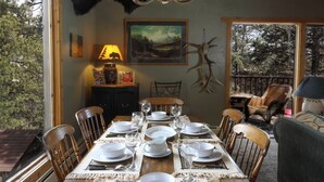 A dining room with a wooden table set for six, a mounted deer head on the wall, and a view of the outdoors through large windows. - Rejuvenation Mountian, Estes Park CO (Estes Park)