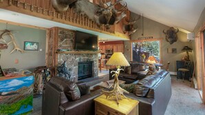 A spacious living room with a stone fireplace, leather sofas, and a mounted deer head. - Rejuvenation Mountian, Estes Park CO (Estes Park)