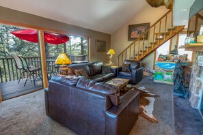 A spacious living room with a leather sofa, a coffee table, and a red umbrella. There is a staircase leading to an upper level, and a painting on the wall.