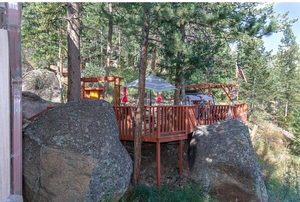 A wooden deck with a metal roof, surrounded by large rocks and trees.