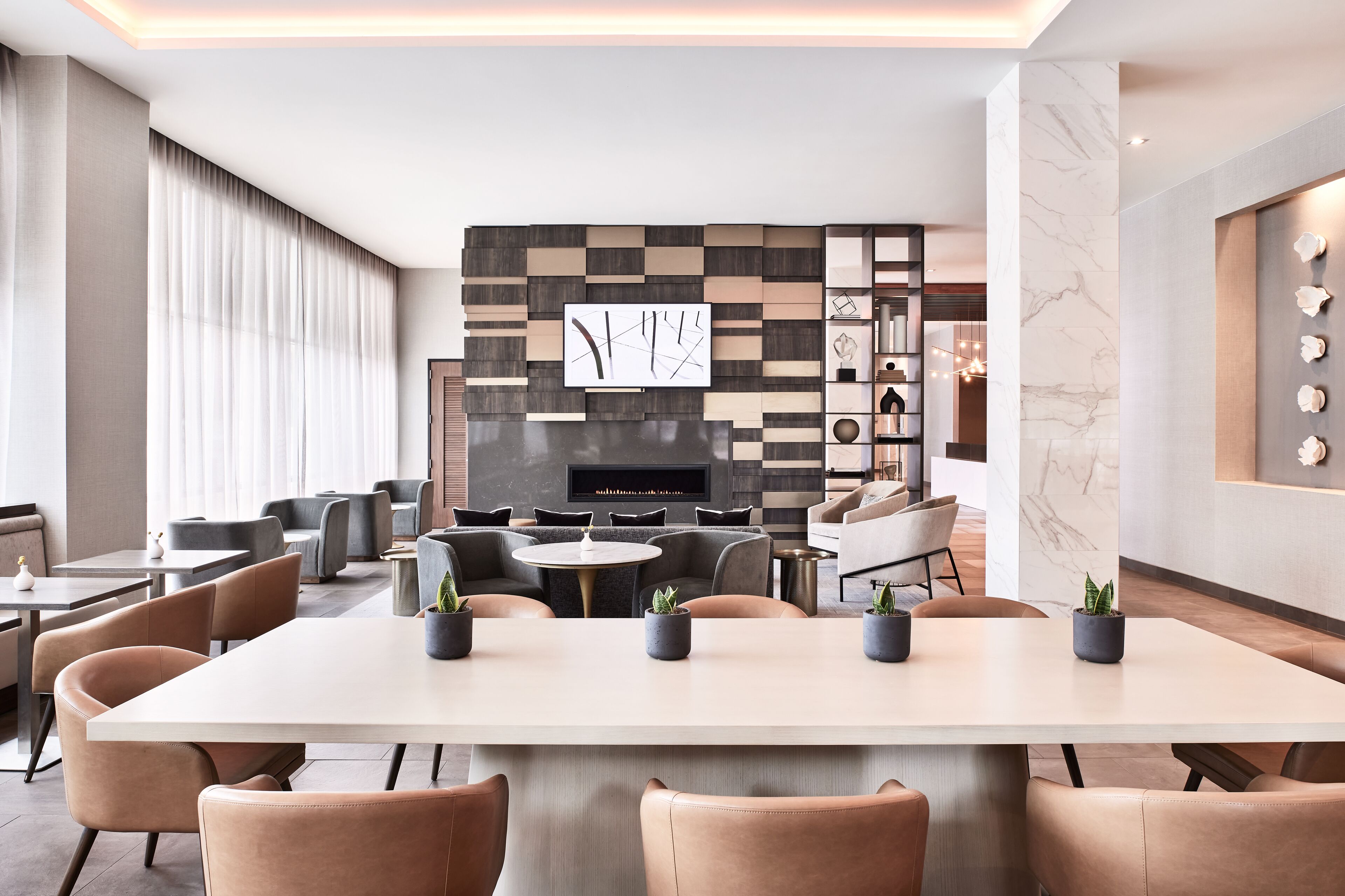 A modern lounge area with a large table, comfortable seating, a fireplace, and a decorative wall.