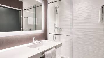 A modern bathroom with a large mirror, a white sink, and a glass-enclosed shower area.