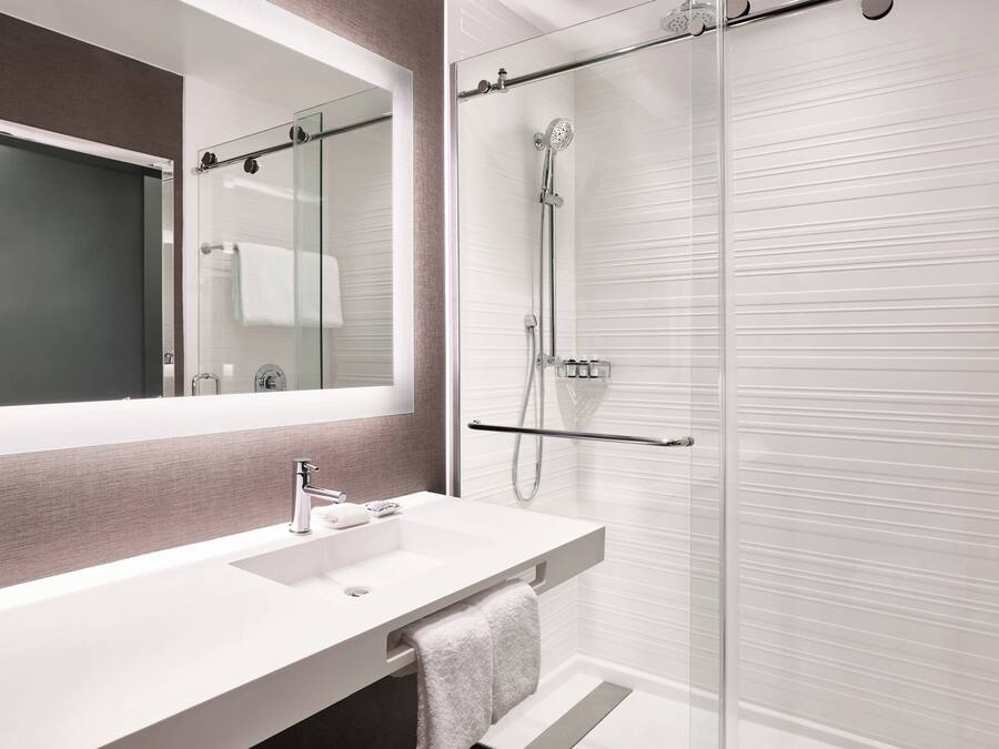 A modern bathroom with a large mirror, a white sink, and a glass-enclosed shower area.
