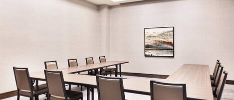 A conference room with a long table and multiple chairs, a framed picture on the wall, and a carpeted floor.