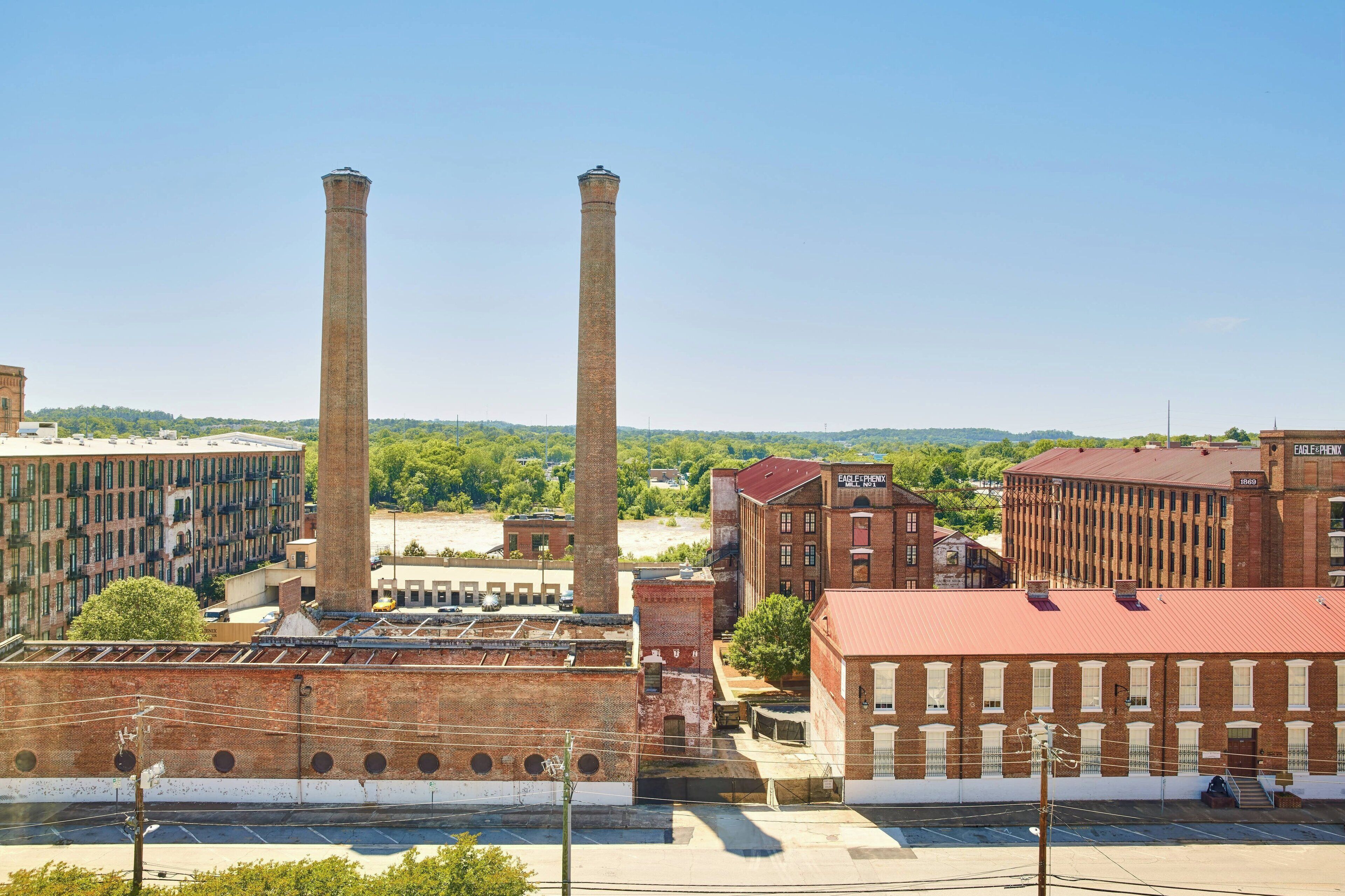 Zona industrial con edificios de ladrillo, dos chimeneas altas y un estacionamiento.