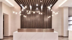 A reception area with a marble reception desk, wooden panel wall, and modern lighting fixtures. - AC Hotel by Marriott Columbus Downtown (Columbus)