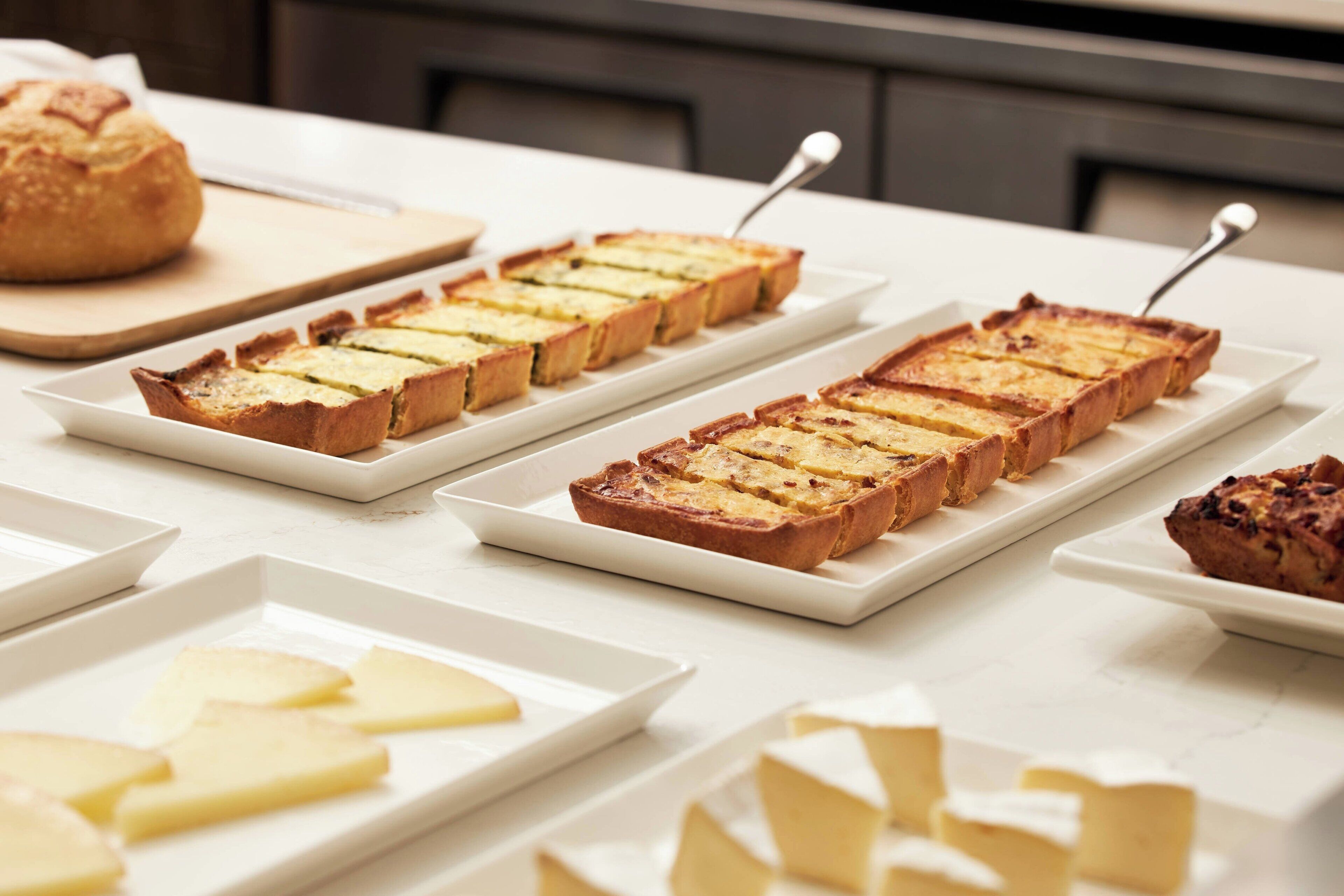 A buffet table with various food items including bread, cheese, and a loaf of bread.
