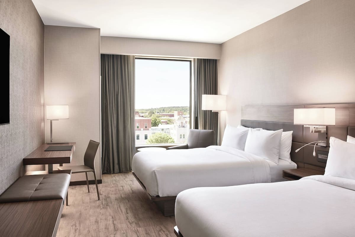 Una habitación de hotel con dos camas, un escritorio, una silla y vistas a la ciudad.