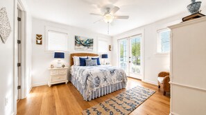 Un dormitorio con cama, mesitas de noche, ventilador de techo y vistas por la puerta.
