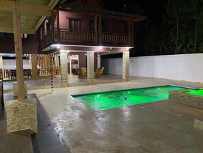 Ein zweistöckiges Haus mit überdachter Terrasse und Swimmingpool.