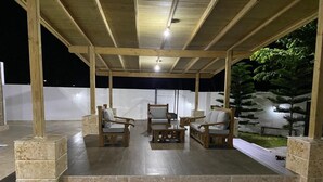 Un'area esterna con posti a sedere in legno e pavimento in pietra, circondata da un muretto e un piccolo giardino.