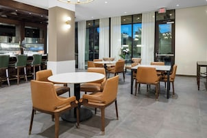 Un comedor moderno con mesas redondas y sillas de cuero, ventanas grandes con cortinas y una zona de bar al fondo.